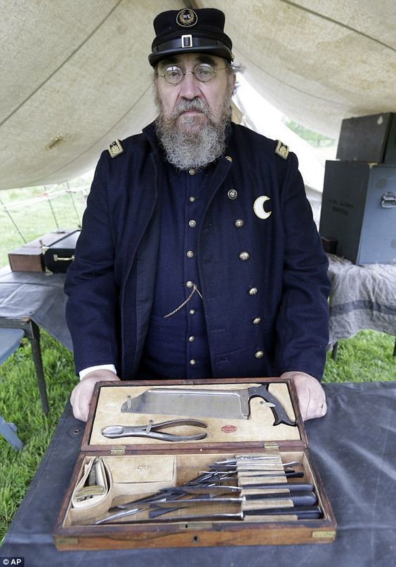 a man in uniform holding an open box with knives and other items inside it under a tent