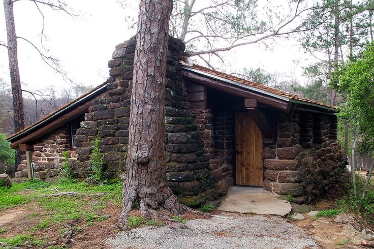 an old log cabin in the woods with stone walls and door, surrounded by trees