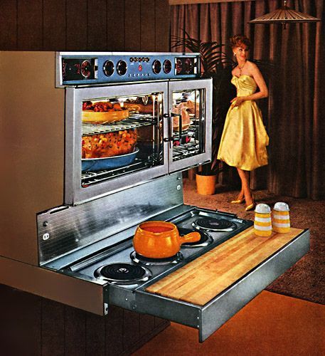 a woman in a yellow dress standing next to an oven with food cooking on it