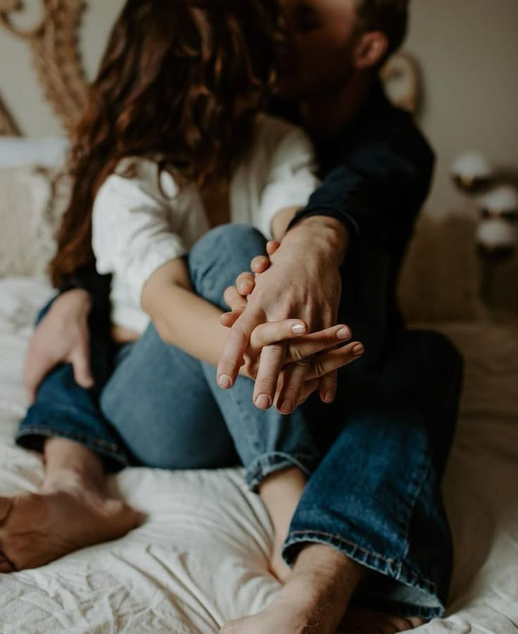 a man and woman sitting on top of a bed holding each other's hands