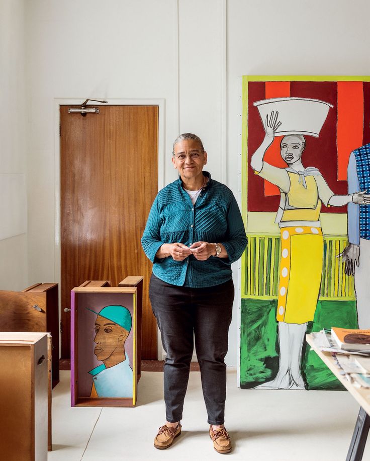 an older woman standing in front of some art on the wall and paintings behind her