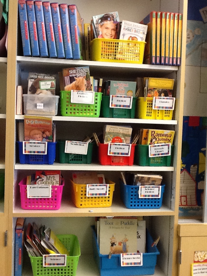 a book shelf filled with lots of books and plastic baskets on top of ...