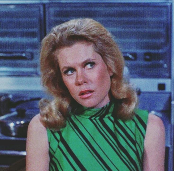 a woman with blonde hair wearing a green dress in front of a stove top oven