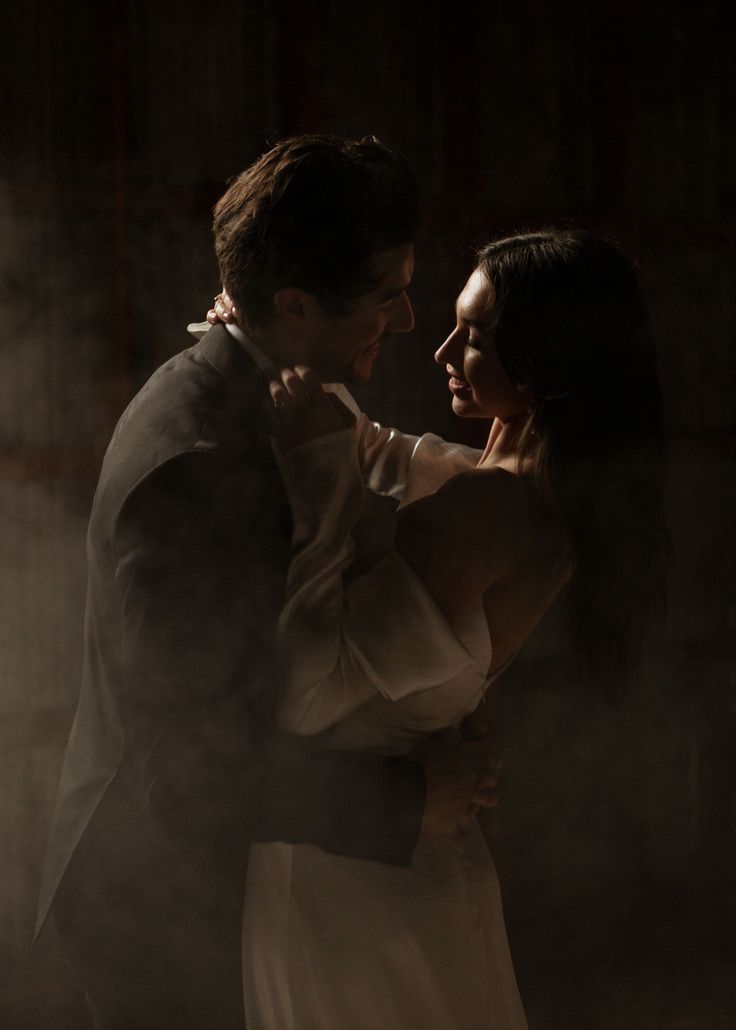 a man and woman standing next to each other in front of a fog filled wall