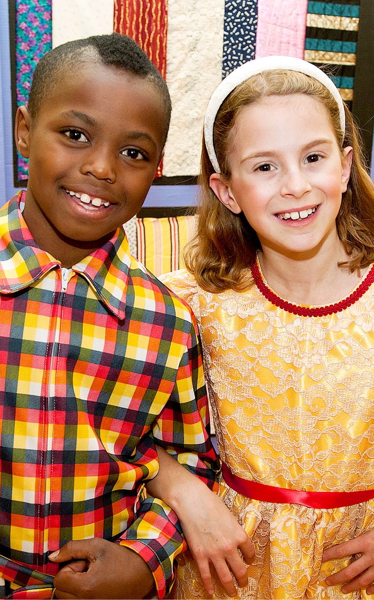 two young children standing next to each other in front of quilts on the wall