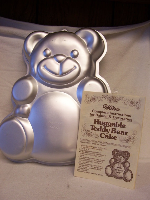 a teddy bear shaped cake pan sitting on top of a white table cloth next to a cookie sheet