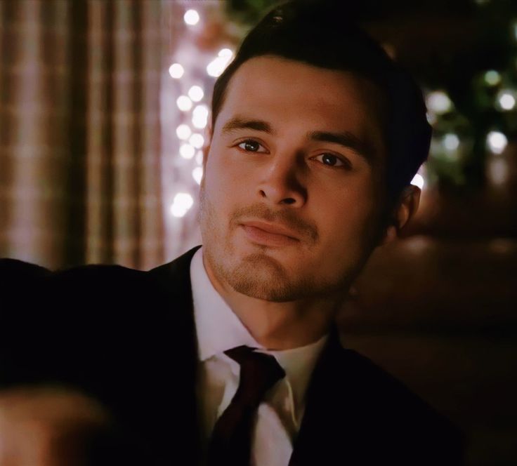 a man wearing a suit and tie in front of a christmas tree with lights on it