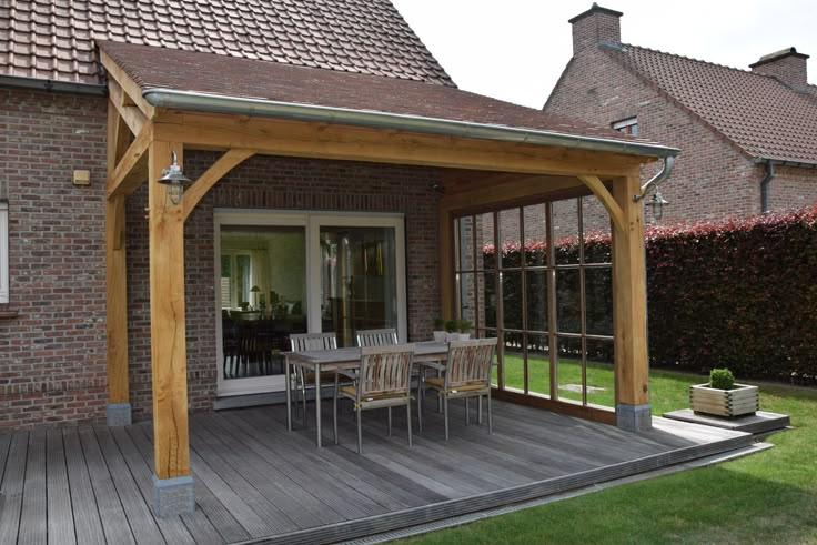 a wooden patio with table and chairs in front of a brick building on the grass