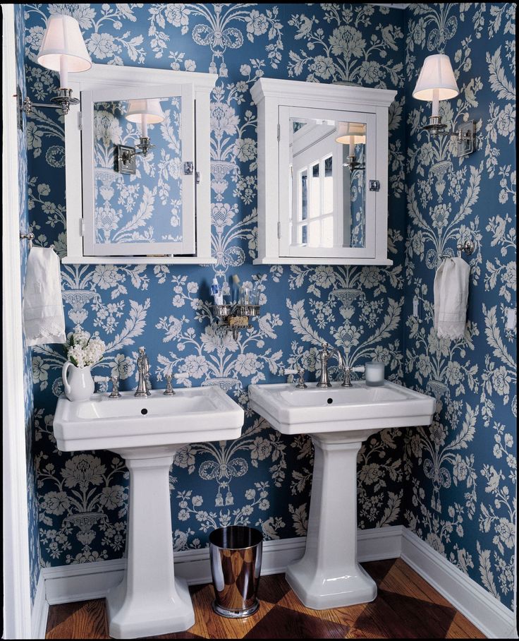 two white pedestal sinks in front of blue wallpapered bathroom with mirror above them