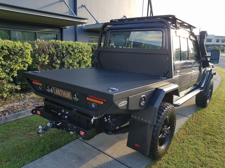 a black truck parked on the side of a road next to a grass covered sidewalk