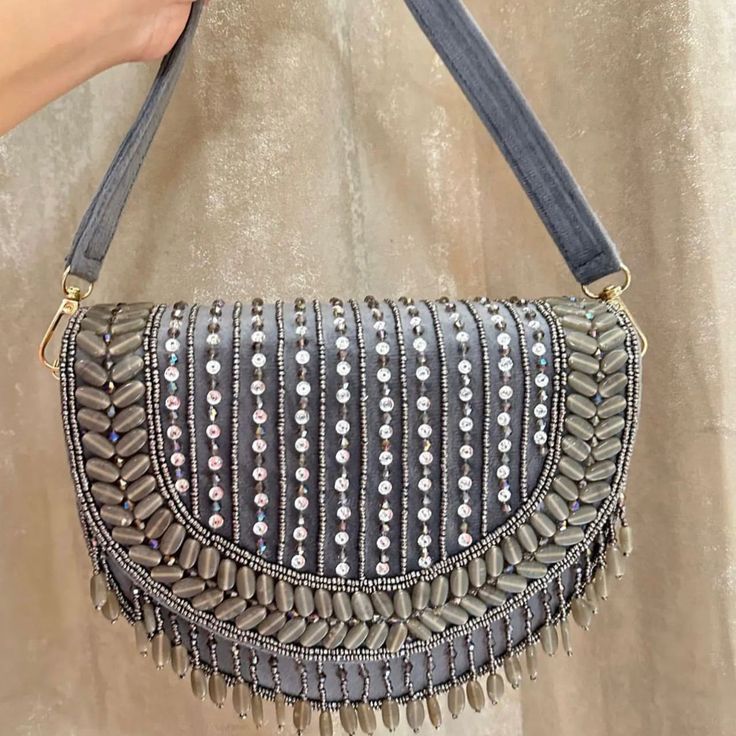 Introducing the Grey Shefali Flap Bag, a stunning fusion of elegance and Indian craftsmanship. Hand-beaded with luxurious velvet in enchanting hues of Grey, this bag embodies opulence and tradition. Its intricate design, coupled with delicate Grey bead work, this makes it a standout accessory for brides and lovers of Indian fashion alike. Whether for a wedding ceremony or a cultural celebration, the Shefali Grey Flap Bag adds a touch of regal charm to any outfit. Elevate your ensemble with the e Luxury Hand Embellished Festive Bag, Silver Embellished Shoulder Bag, Bohemian Style Shoulder Bag For Evening Festivals, Bohemian Shoulder Bag For Evening Festivals, Bohemian Embellished Clutch Shoulder Bag, Bohemian Evening Shoulder Bag For Festivals, Embroidered Bags For Party And Festival, Elegant Festival Bags, Elegant Silver Bag For Festivals