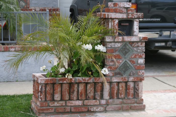 a brick planter with white flowers in it on the side of a road next to a car