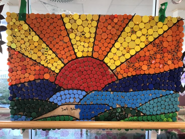 an art piece made out of bottle caps with the sun setting in the sky behind it