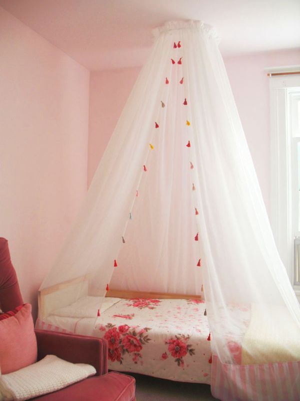 a white canopy bed in a pink room with flowers on the bedspread and pillows