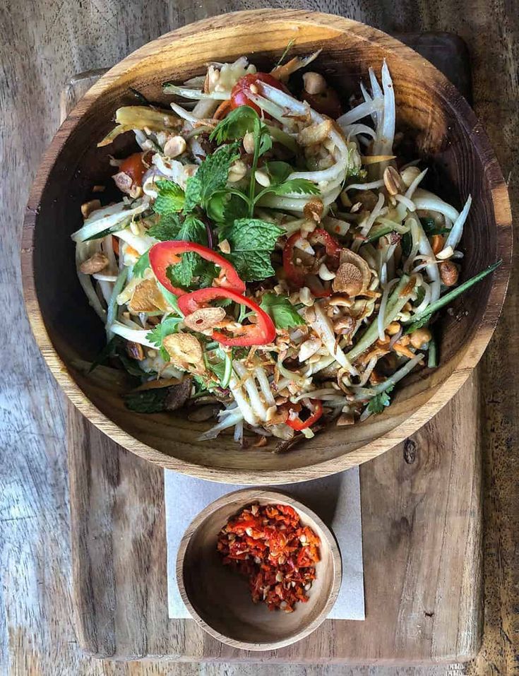 a wooden bowl filled with salad on top of a table next to a small bowl of seasoning