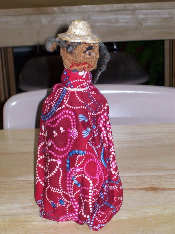 a small doll wearing a red dress and hat on a wooden table next to a white chair