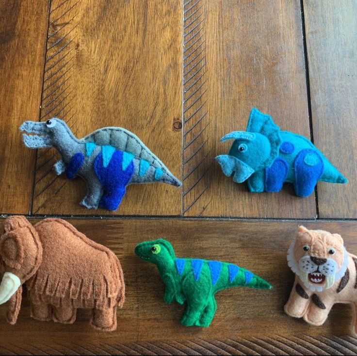 four felt dinosaurs sitting on top of a wooden floor