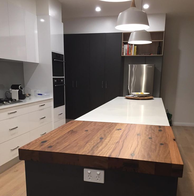 an island in the middle of a kitchen with white cabinets and wood counter tops on both sides