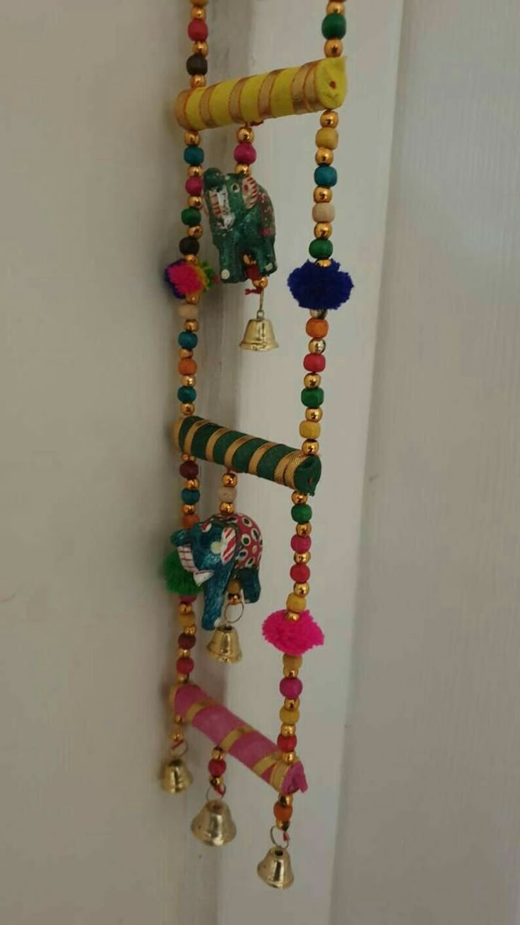 a wall hanging made out of beads and bells with an elephant head on it's side