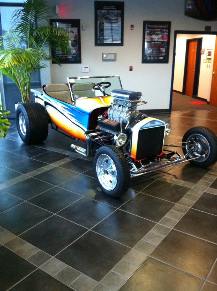 an old model car is on display in a building with black tile flooring and large windows