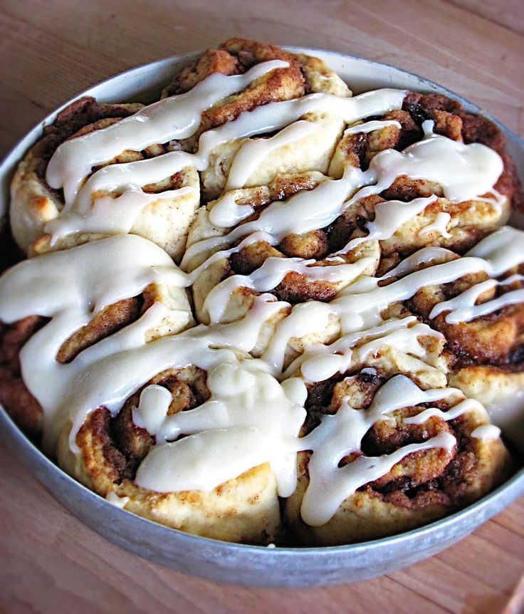 a pan filled with cinnamon rolls covered in white icing on top of a wooden table