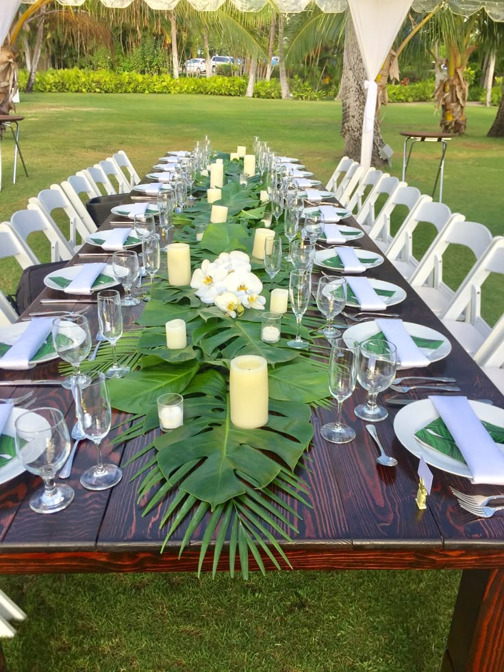 a long table set with place settings and candles on it for an outdoor dinner party