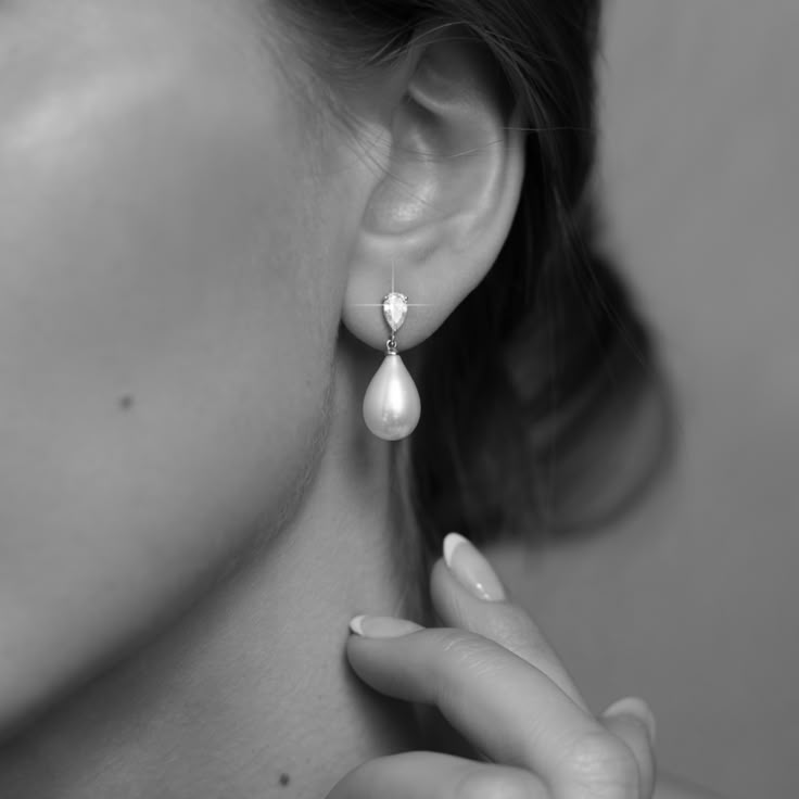 a woman is holding her ear up to the side while wearing earrings with pearls on them