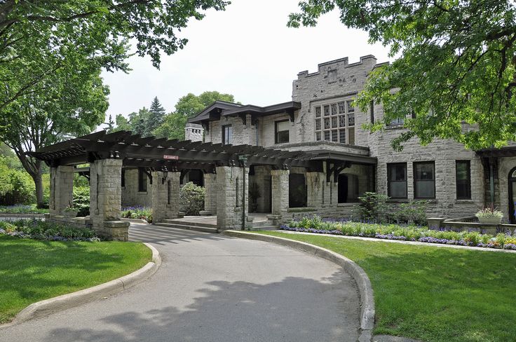 a large stone house with an attached pergolated walkway and trees in the front yard