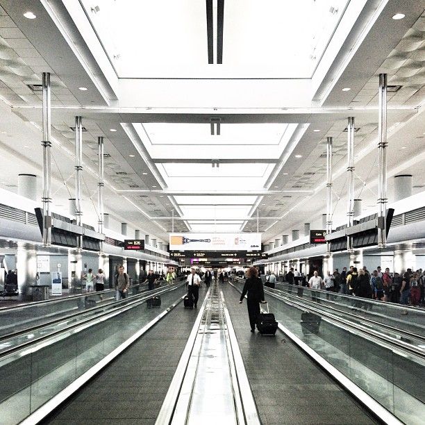 an airport filled with lots of people walking through the walkways and escalators