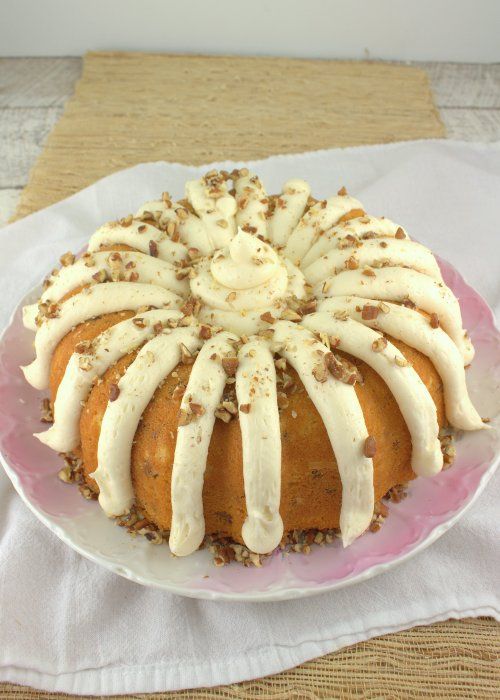 an italian cream bundt cake on a pink plate with white icing and pecans