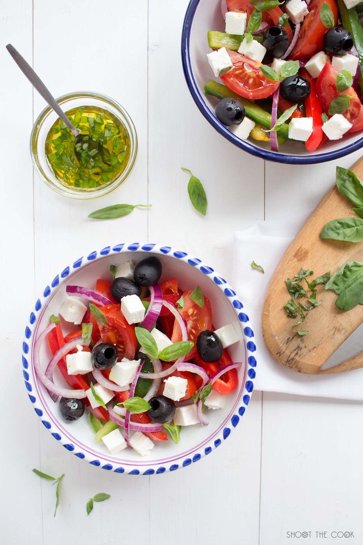 two bowls filled with different types of salads next to a cutting board and knife