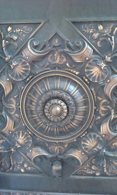 an ornate metal design on the side of a building's door, with flowers and leaves around it