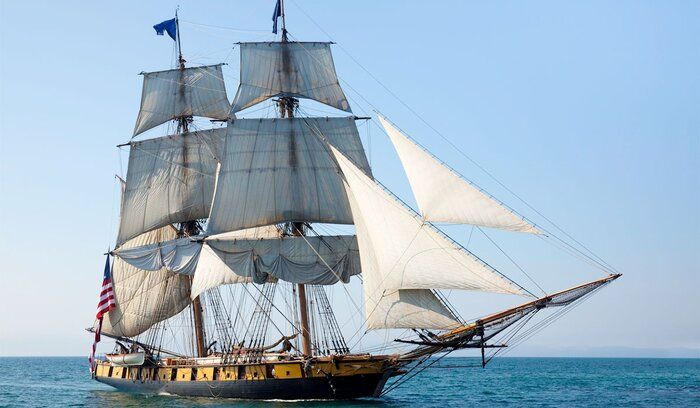 an old sailing ship in the middle of the ocean with white sails and two masts