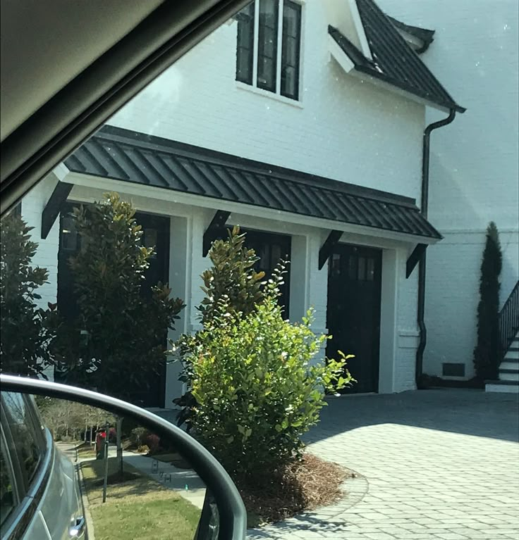 a car is parked in front of a white house with black shingled roof and windows