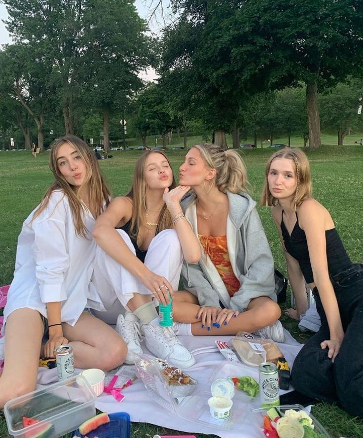 four women sitting on a blanket in the grass eating food and drinking water from bottles