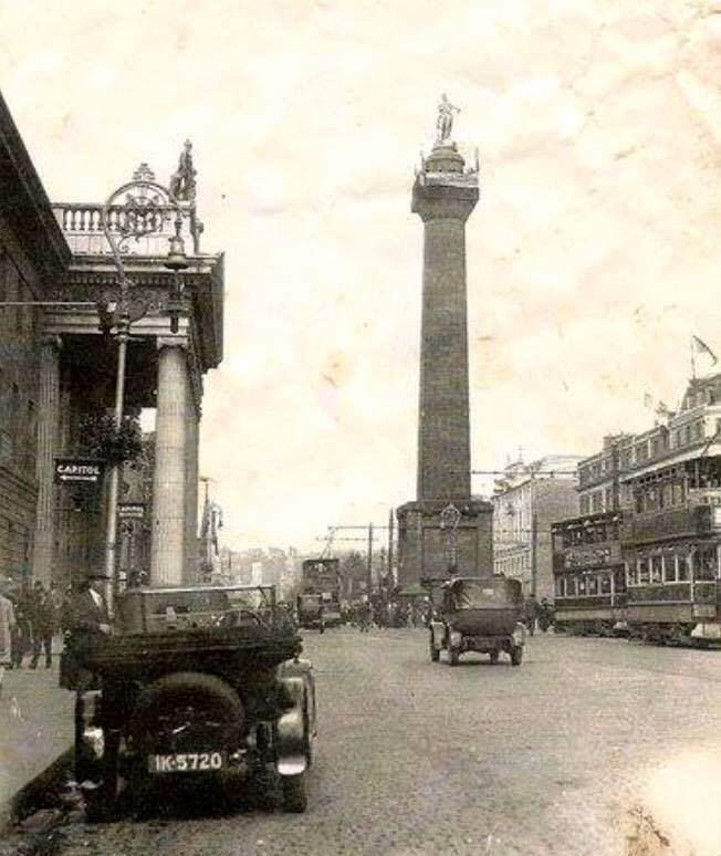 an old black and white photo of a street with cars, buses, and a clock tower in the background