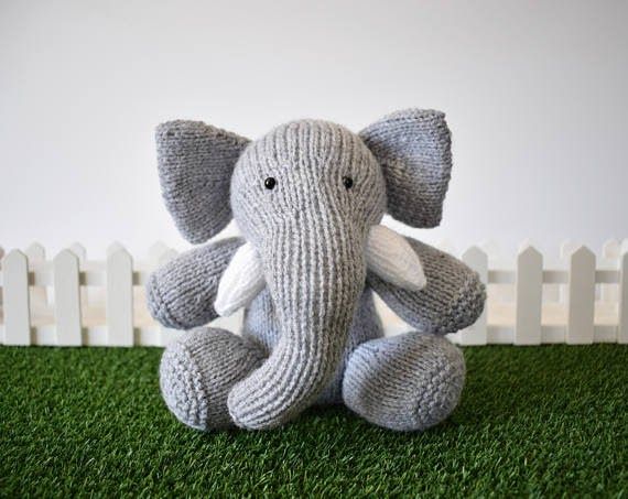 an elephant stuffed animal sitting on top of a green grass covered field next to a white picket fence