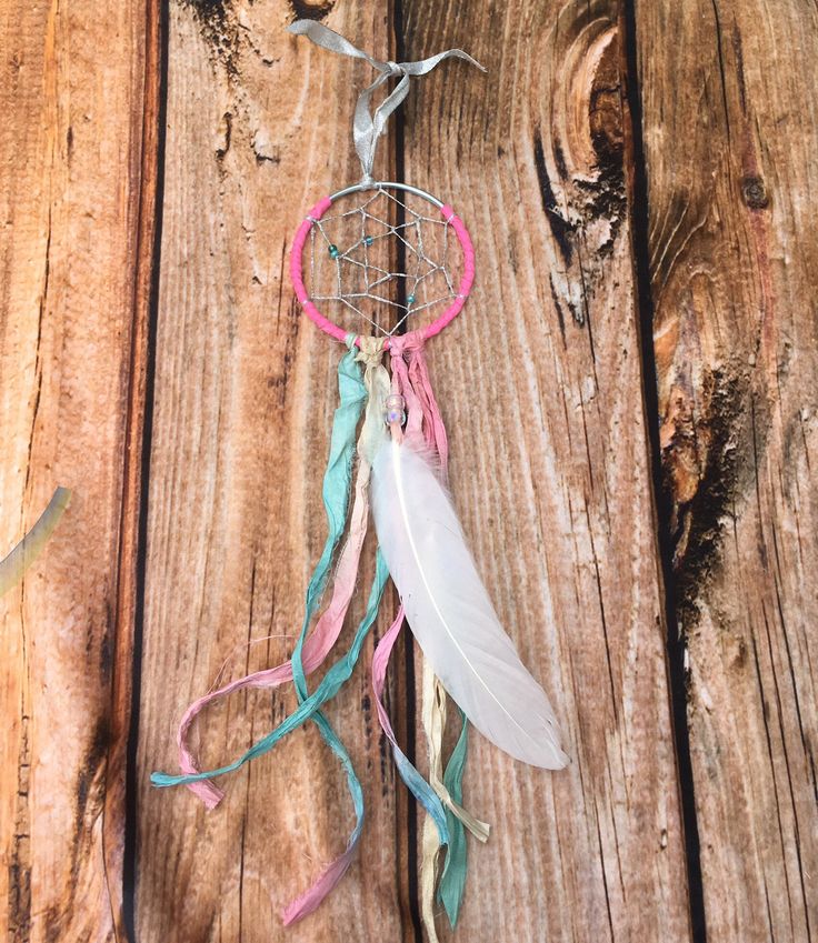 a dream catcher is hanging on a wooden wall with feathers and ribbons attached to it