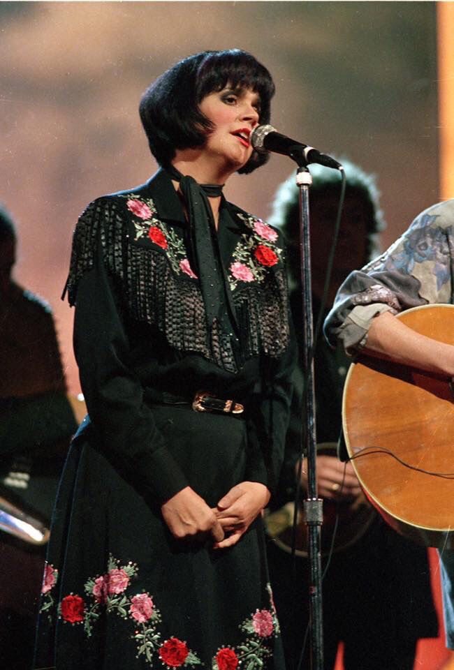 a woman singing into a microphone while holding an acoustic guitar in front of a man