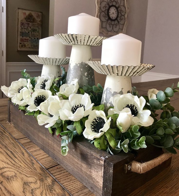 some white flowers and candles are in a wooden box on a table with wood planks