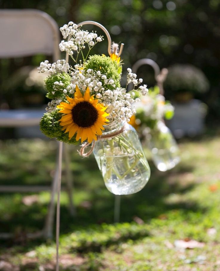 sunflowers and baby's breath in mason jars are hung from the back of chairs