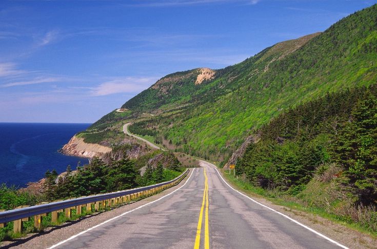 an empty road near the ocean with mountains in the background