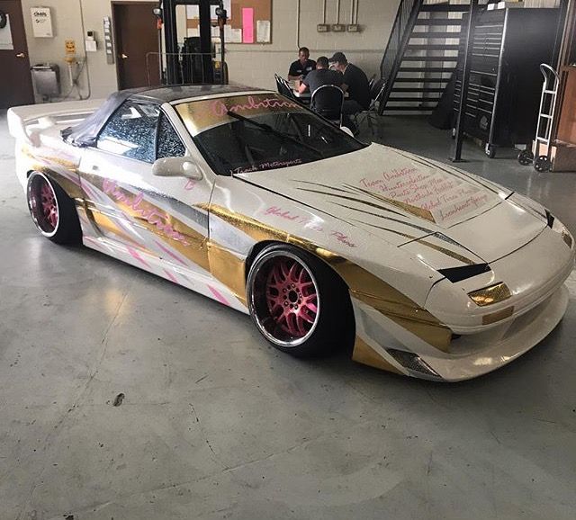 a gold and white car parked in a garage with people sitting at tables behind it