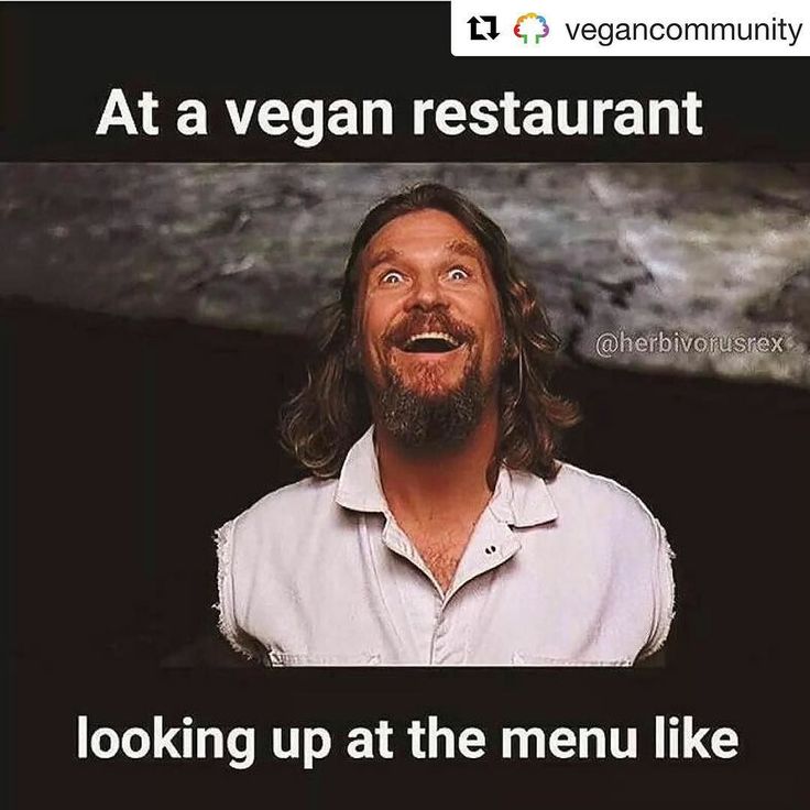 a man with long hair and beard standing in front of a sign that says, at a vegan restaurant looking up at the menu like