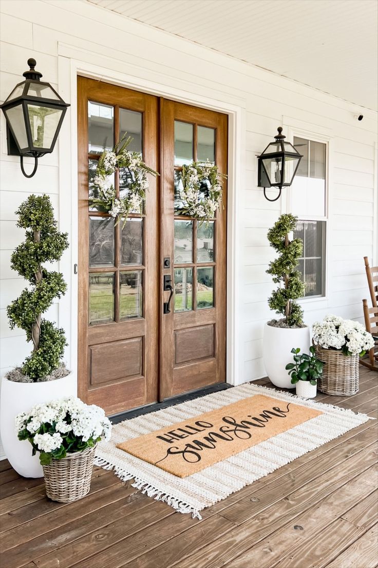 two potted plants are sitting on the front porch with a welcome mat in front