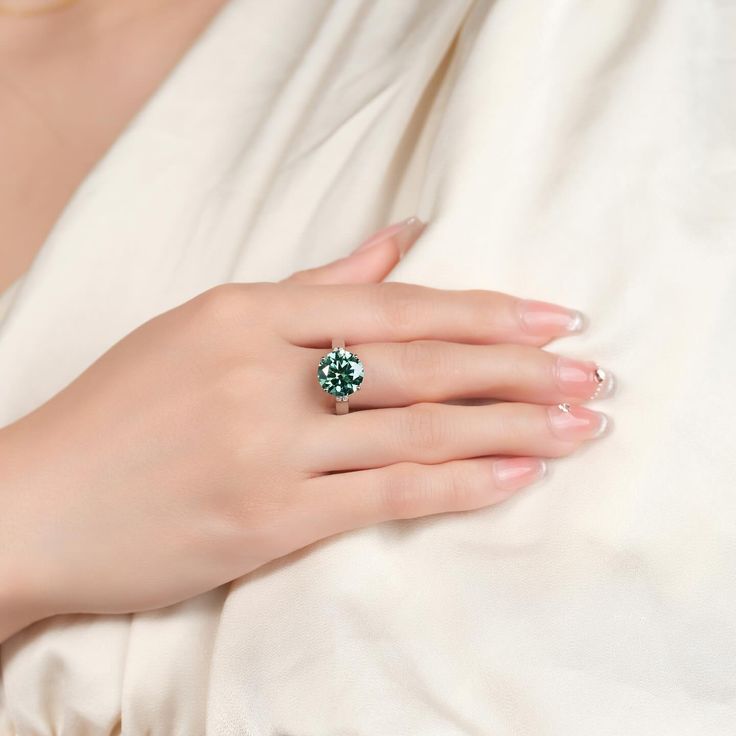 a woman's hand with a green ring on her left wrist, wearing a white dress