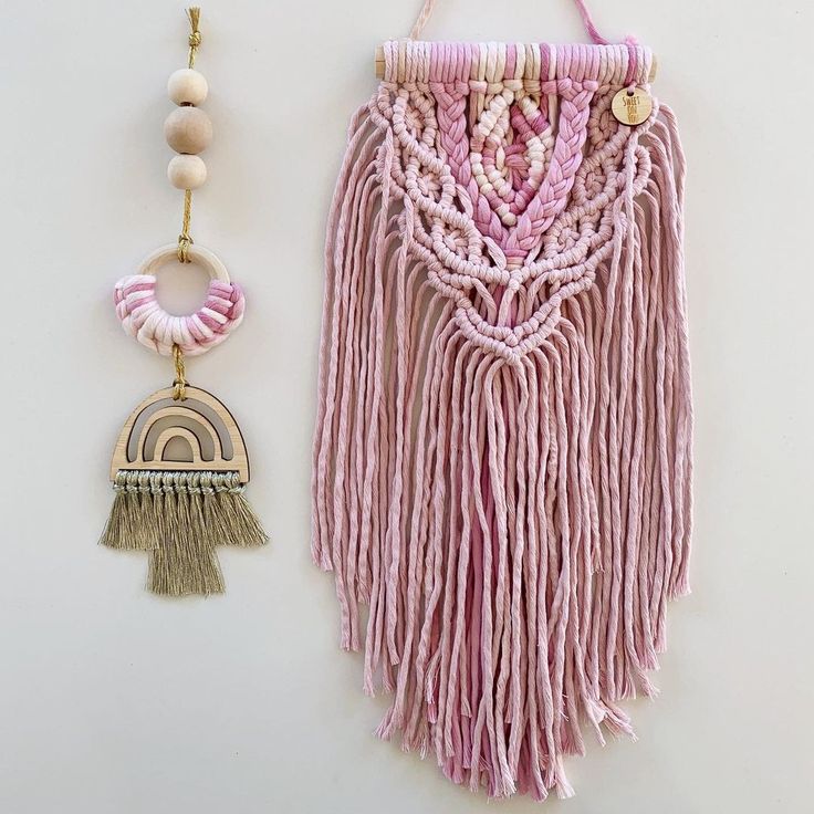 a pink wall hanging next to a wooden bead and tassel necklace on a white background