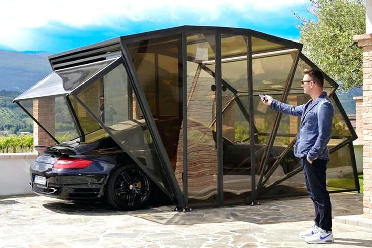 a man standing next to a black car in front of a glass structure with the door open