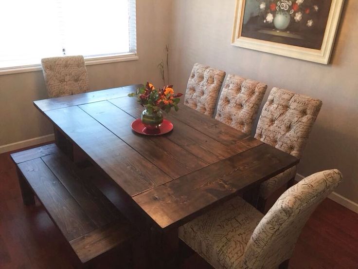 a wooden table with four chairs around it and a vase filled with flowers on top