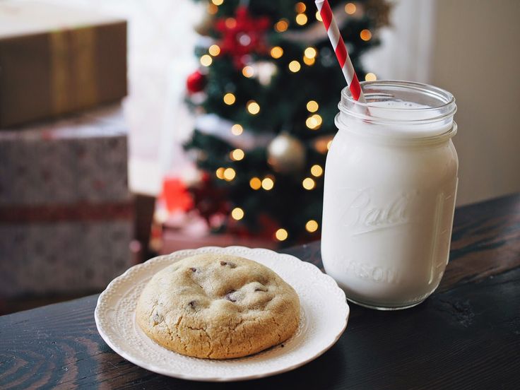 a cookie on a plate next to a glass of milk and a christmas tree in the background